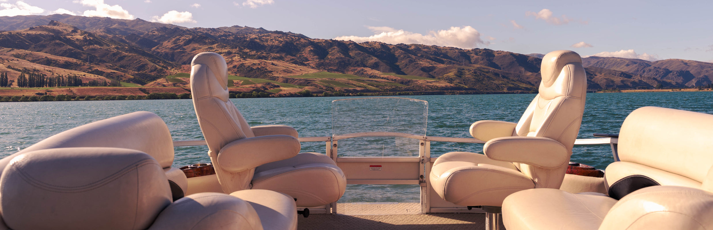 Beige recliner chairs on a boat with a scenic background of water and hills.